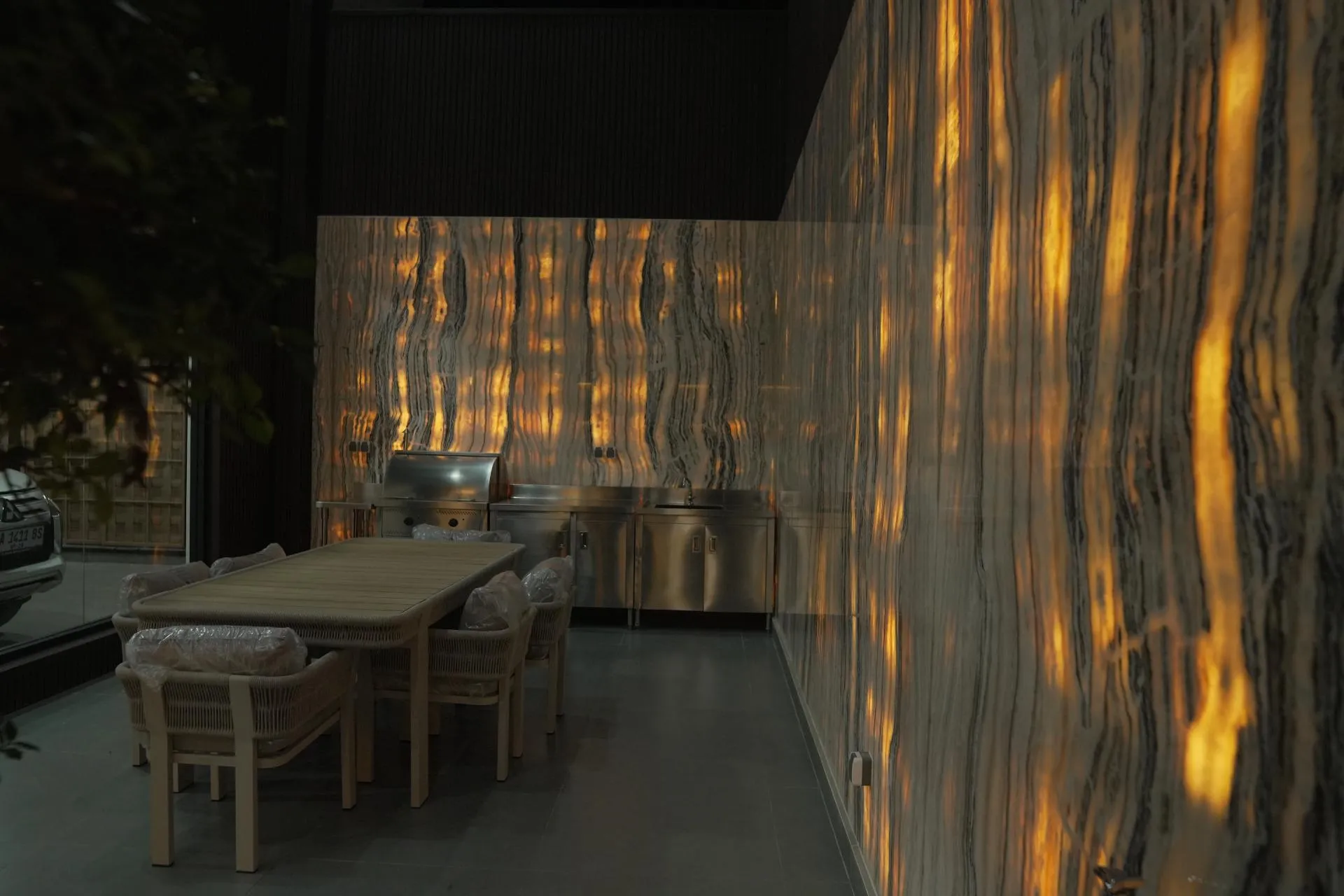 Teras belakang dengan dapur luar stainless dan dinding onyx bercahaya dari belakang